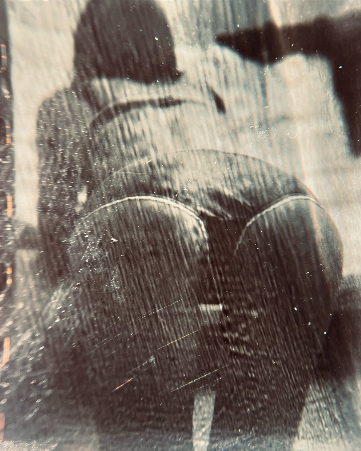Abstract view of a person bending over, captured in a high-contrast, grainy black and white photograph with visible surface scratches.