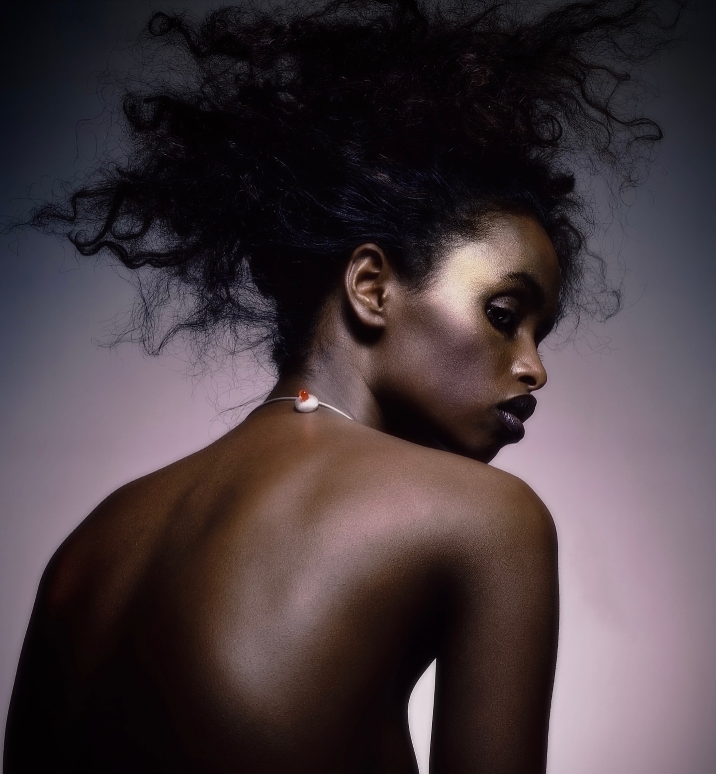 Elegant portrait of a Black woman with striking dark hair, visible back, and subtle necklace against a gradient grey and pink backdrop.
