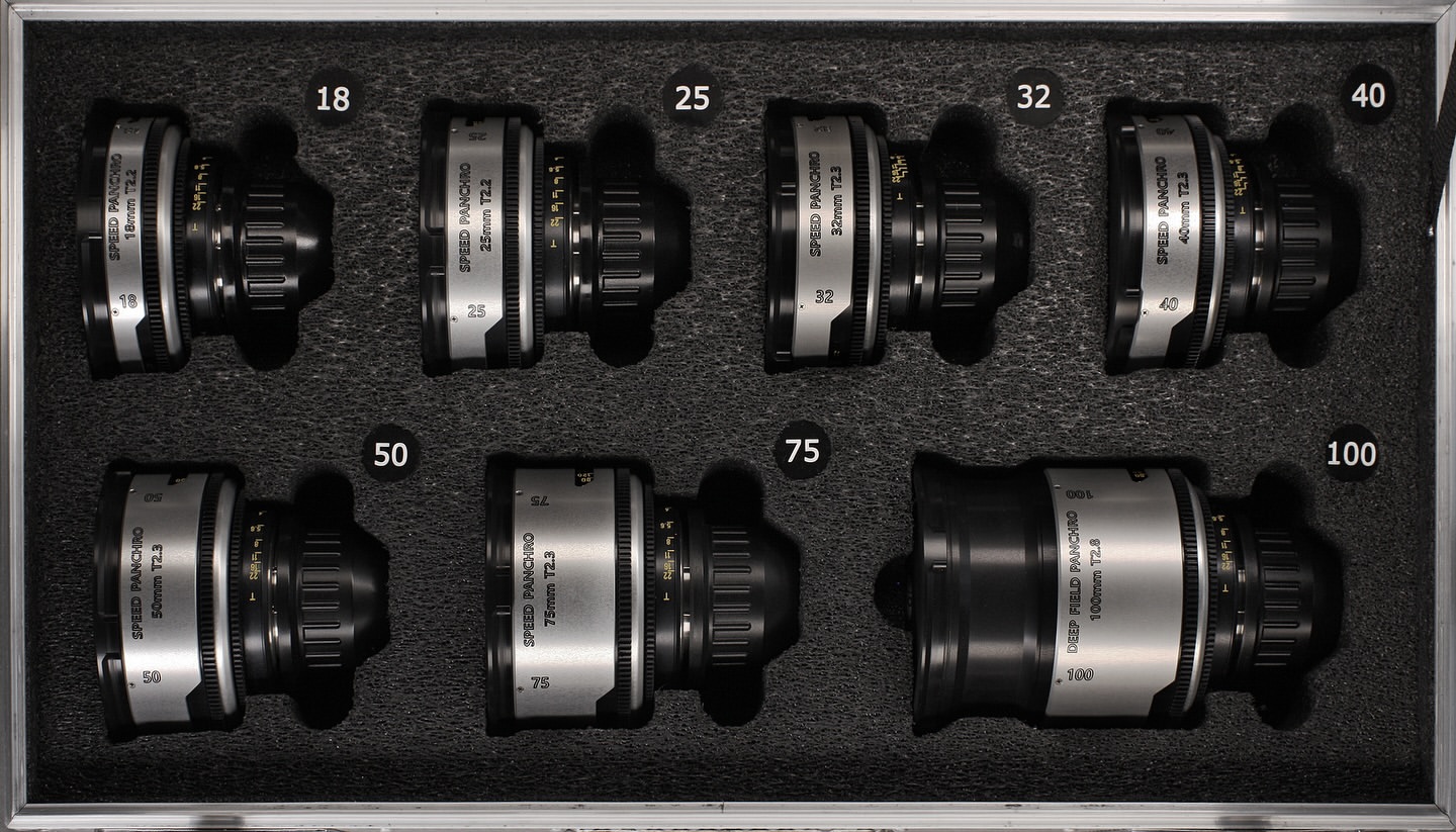 Eight camera lenses of varying focal lengths displayed in a fitted protective case, ranging from 18mm to 100mm, with visible text labels.