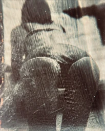 Monochrome low angle grainy photographic portrait of a seated person with textured vertical streaks across the frame.