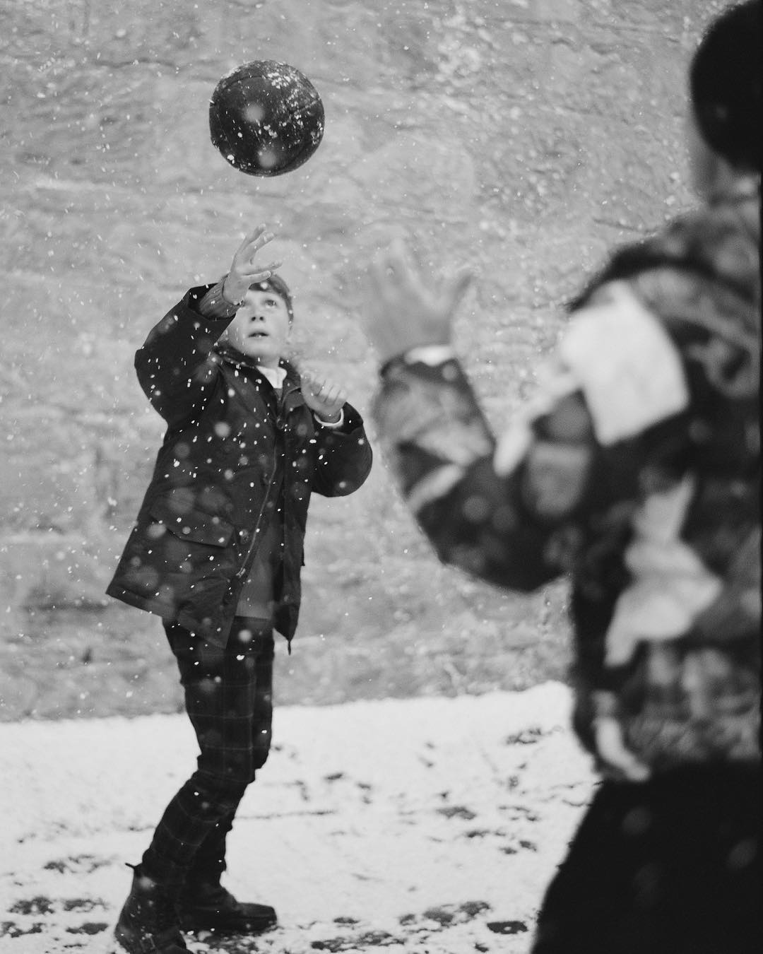 A boy throws a ball in a black and white shot, the image captures the moment the ball leaves his hands on a snowy day.