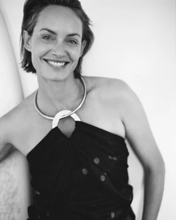 Portrait of a smiling woman wearing a dark strapless top and a prominent silver collar necklace against a light background.