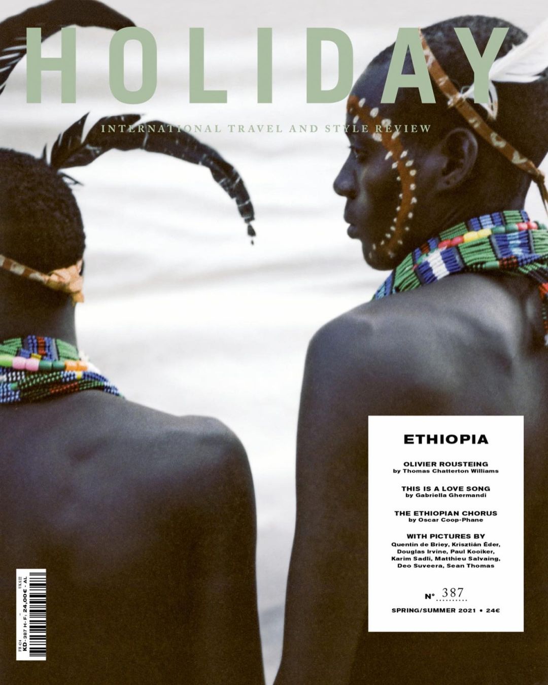 Magazine cover featuring two men with dark skin, adorned with traditional tribal accessories, against a blurred white background. The magazine is titled HOLIDAY.