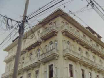 Exterior view of a vintage building with balconies, featuring an upward angle and visible power lines against a clear, neutral sky.