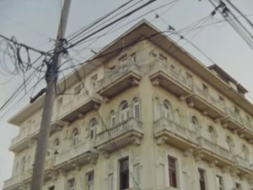 Exterior view of a vintage building with balconies, featuring an upward angle and visible power lines against a clear, neutral sky.
