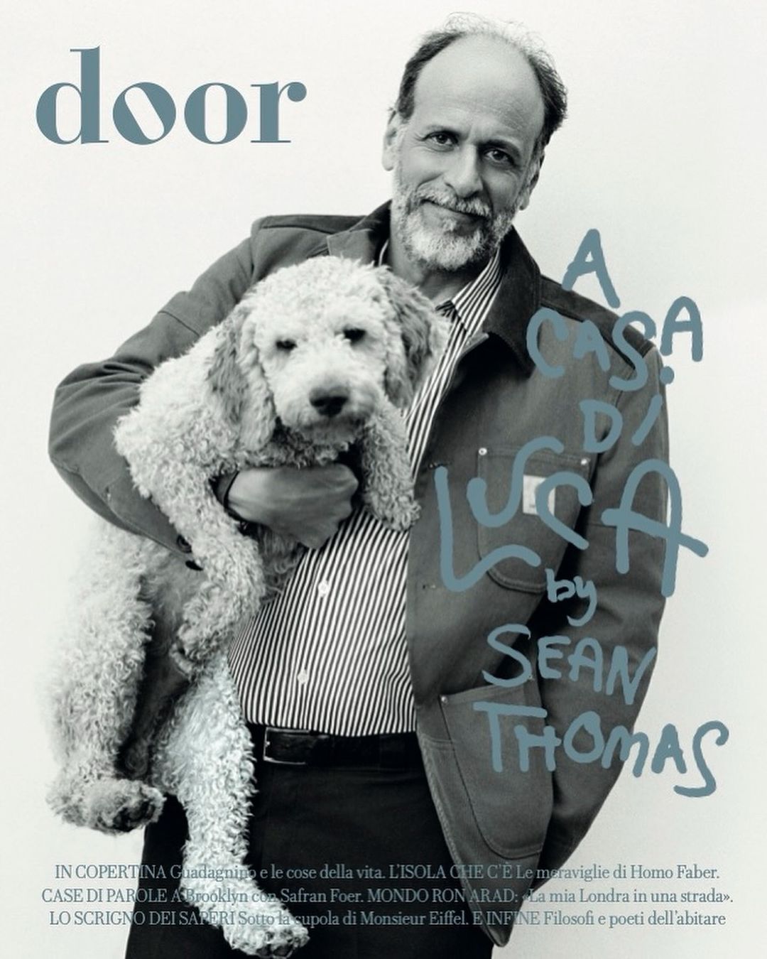 Portrait of an adult man holding a white standard poodle, wearing a striped shirt and casual jacket, in a photo studio setting for a magazine cover.