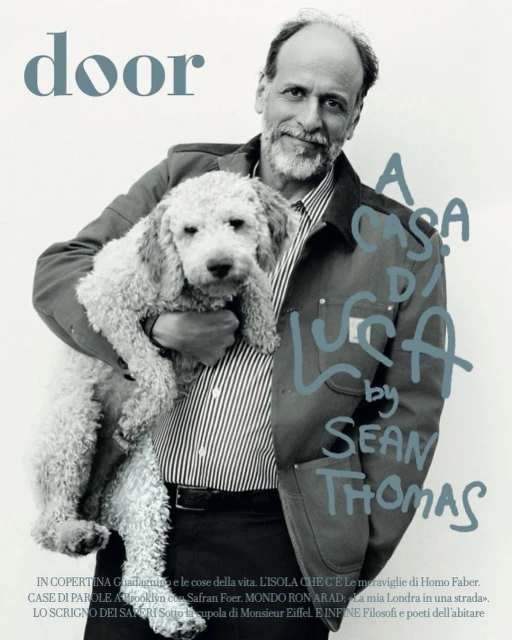 Portrait of an adult man holding a white standard poodle, wearing a striped shirt and casual jacket, in a photo studio setting for a magazine cover.