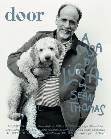 Portrait of an adult man holding a white standard poodle, wearing a striped shirt and casual jacket, in a photo studio setting for a magazine cover.