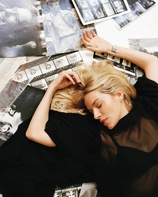 Woman lying on a surface covered in black and white photographs and film negatives, posing and wearing a black mesh top.