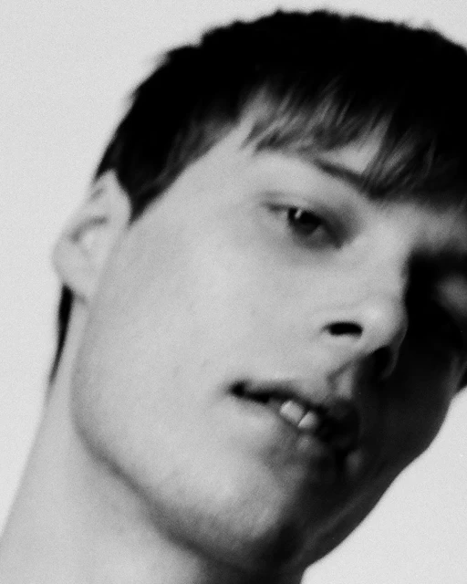 Monochromatic close-up portrait of a fair-skinned adult male with short dark hair, featuring a neutral expression and bright, even lighting.