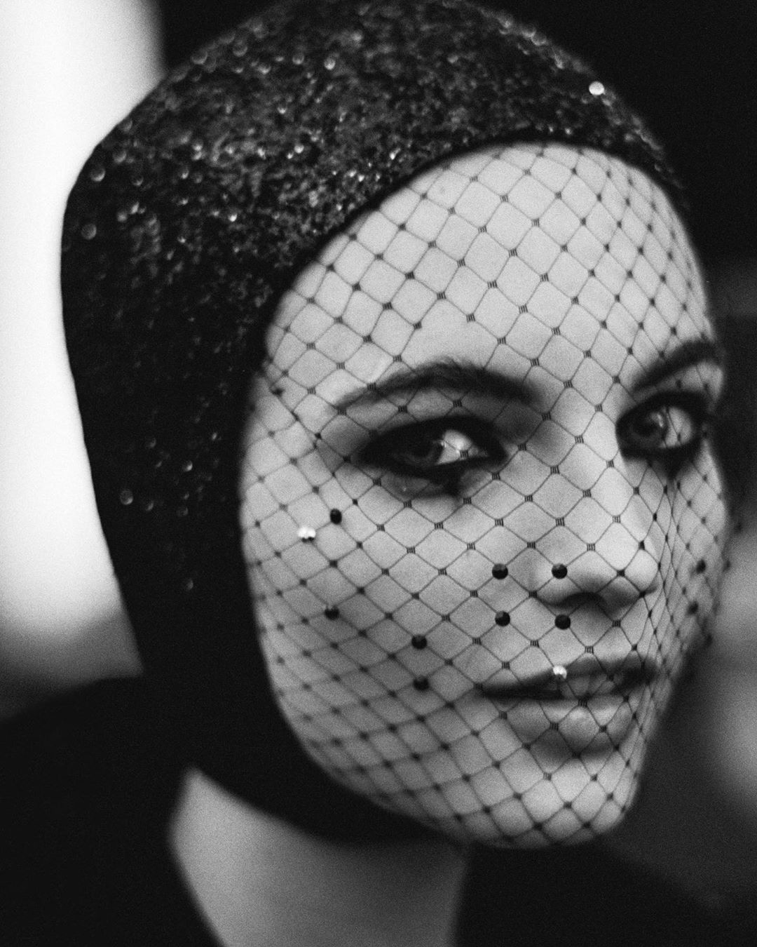 Monochrome portrait of a woman wearing a sequin hat and beaded net veil, showcasing beauty and fashion in a studio setting.