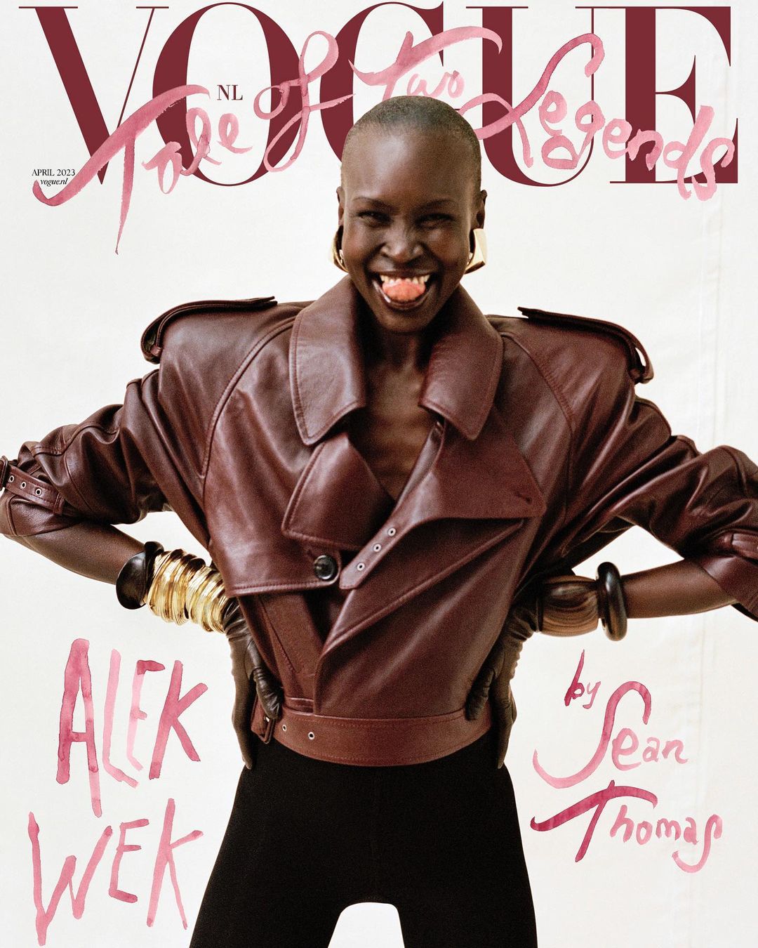 Vogue NL cover featuring Alek Wek wearing a brown leather jacket, gold bracelets, black leggings, and big gold hoop earrings smiling.