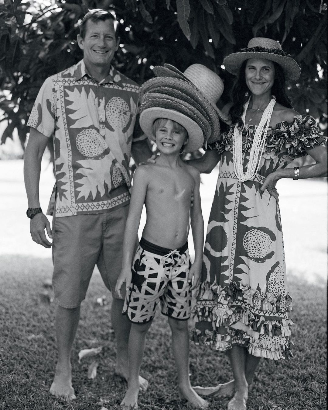 Black and white portrait of a family of three posing outdoors, including an adult male, adult female and a child in straw hats.