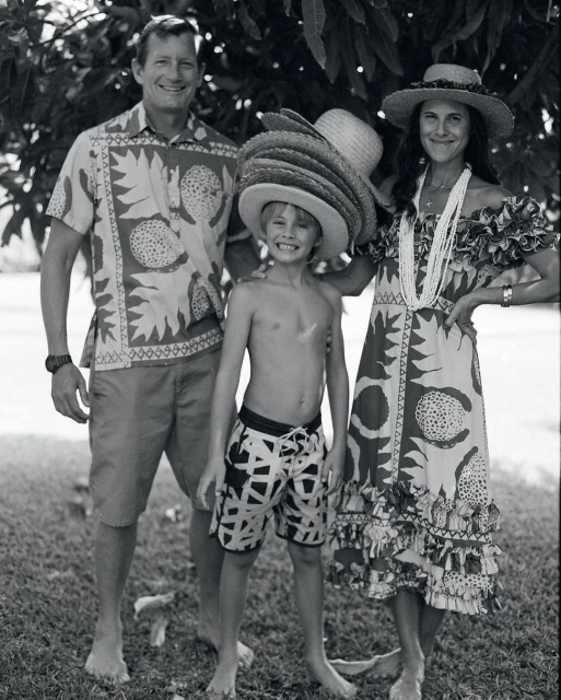 Black and white portrait of a family of three posing outdoors, including an adult male, adult female and a child in straw hats.