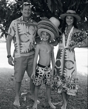 Black and white portrait of a family of three posing outdoors, including an adult male, adult female and a child in straw hats.