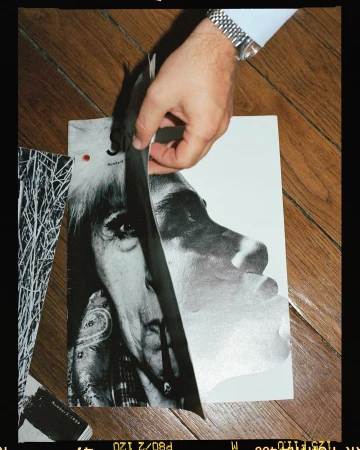 Black and white photo of a man's hands holding pages of a magazine featuring a portrait of an older woman with long hair.