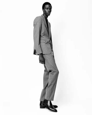 Black man wearing a pinstripe suit and leather boots standing against a plain white background.