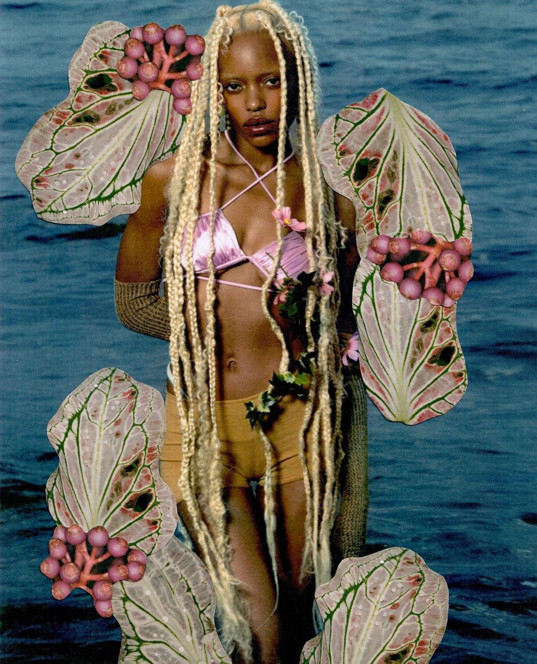 Artistic image of a woman with light blonde hair in a pink bikini top and yellow shorts surrounded by botanical elements and set against water.