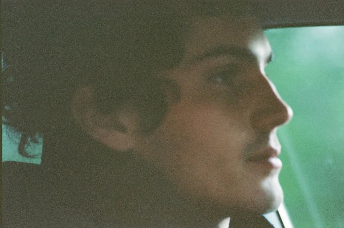 Profile of a young adult male in car looking toward window with natural light, soft focus, and green hues.
