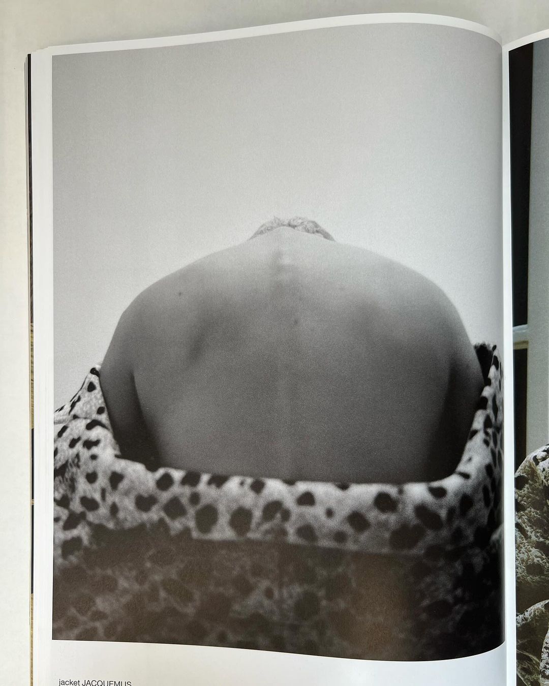 Black and white photo of a person's back and shoulders against a plain wall, draped with a patterned animal-print fabric.