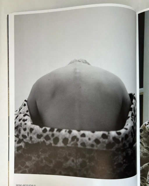 Black and white photo of a person's back and shoulders against a plain wall, draped with a patterned animal-print fabric.