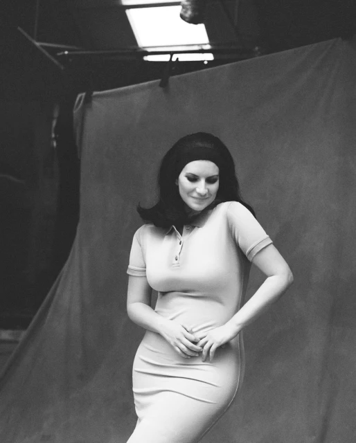 Black and white portrait of an adult woman wearing a polo dress and headband, posing in a studio setting with a draped backdrop.