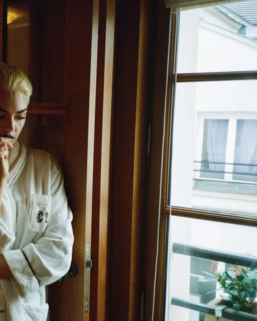 A woman with short blonde hair is partially visible wearing a white robe in a room with natural light from the window behind her.