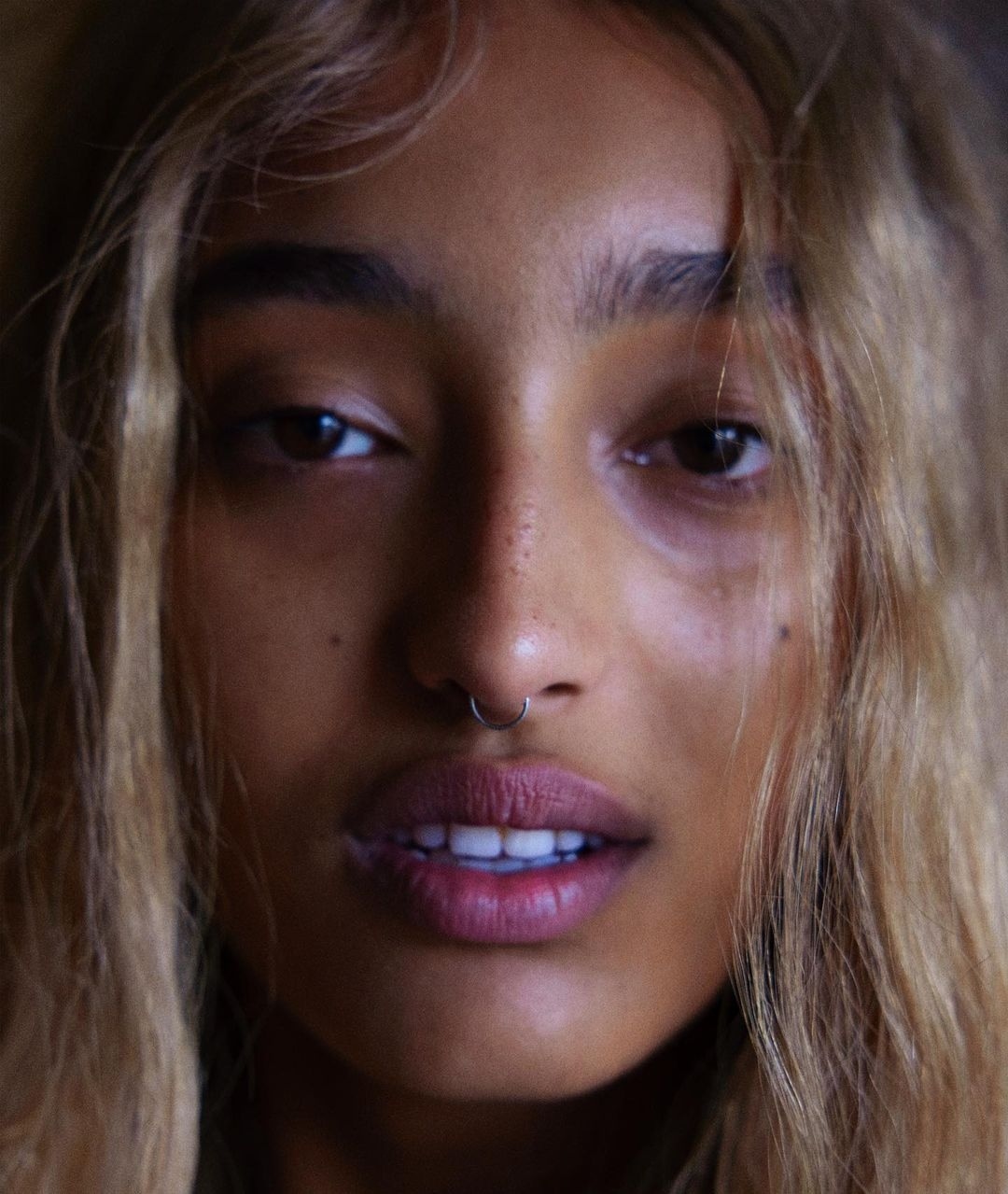 Close-up portrait of an adult female with light brown hair, fair skin, and a nose ring, looking directly at the camera with a neutral expression.