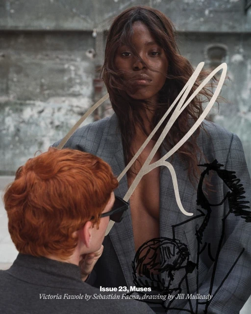 Editorial fashion shot: a woman with brown hair in a grey blazer, accompanied by a red-haired person with glasses and a grey top.