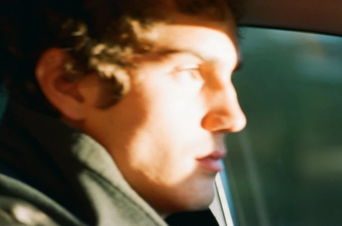 Close up profile portrait of a young man with curly hair driving a car in bright sunlight by Sebastian Faena