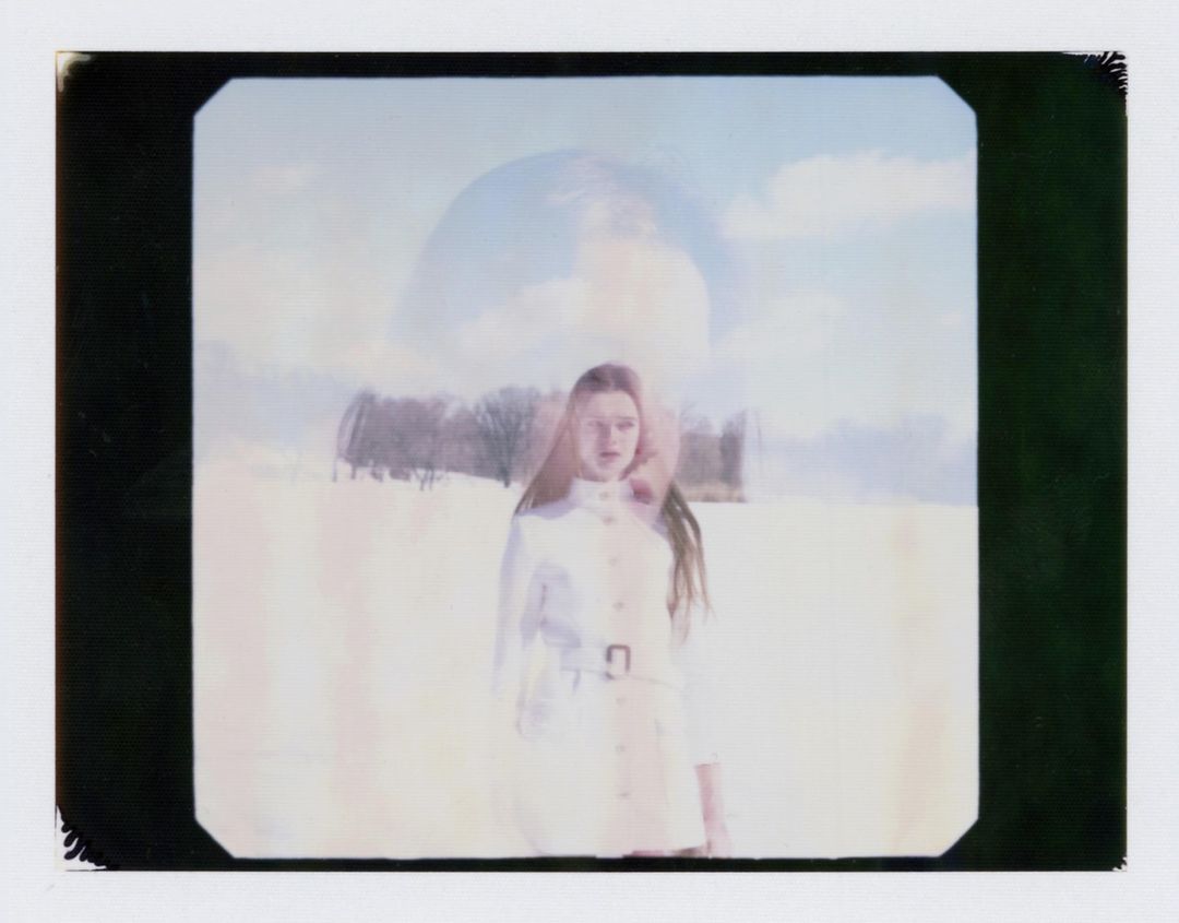 A woman in a white coat poses in a winter landscape with snow and a blurred, artistic style featuring pastel colors and an out-of-focus background.