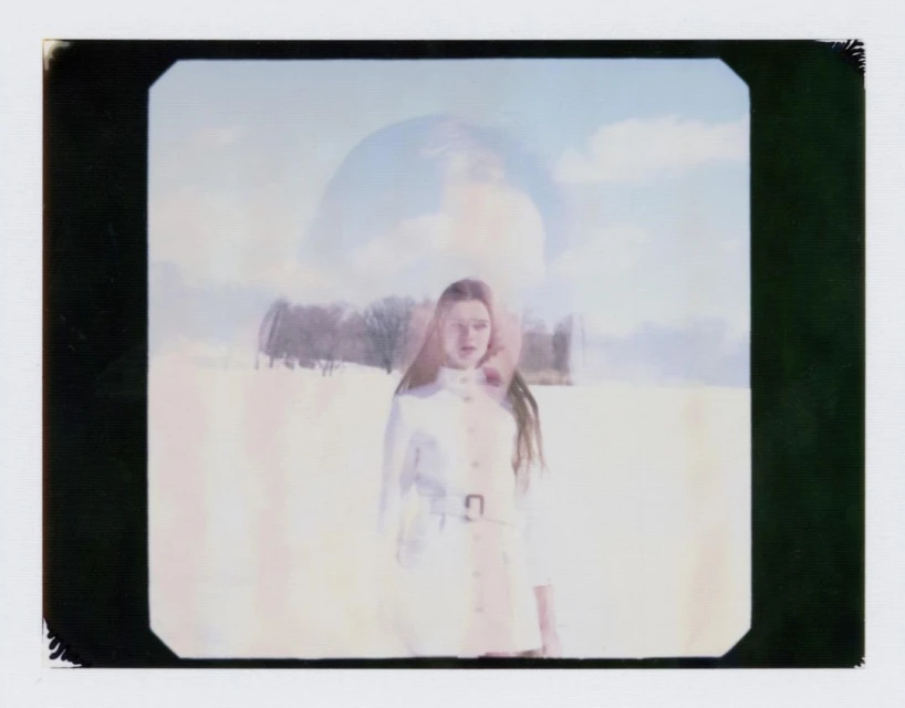 A woman in a white coat poses in a winter landscape with snow and a blurred, artistic style featuring pastel colors and an out-of-focus background.