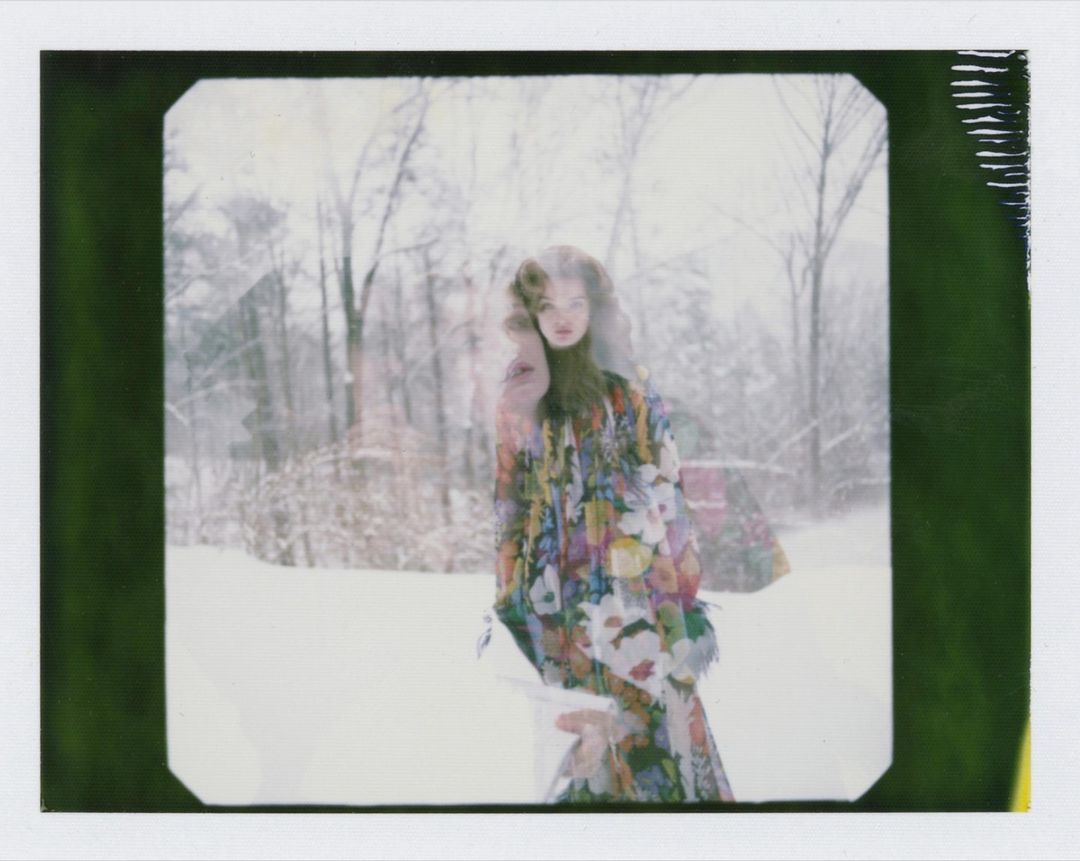 Woman in floral dress stands in a snowy forest with double exposure effect, creating a dreamy, ethereal fashion portrait.