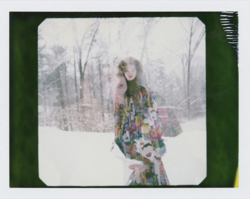 Woman in floral dress stands in a snowy forest with double exposure effect, creating a dreamy, ethereal fashion portrait.