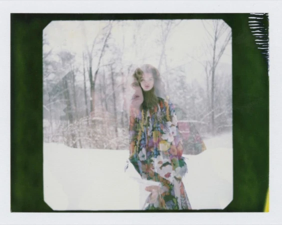 Woman in floral dress stands in a snowy forest with double exposure effect, creating a dreamy, ethereal fashion portrait.