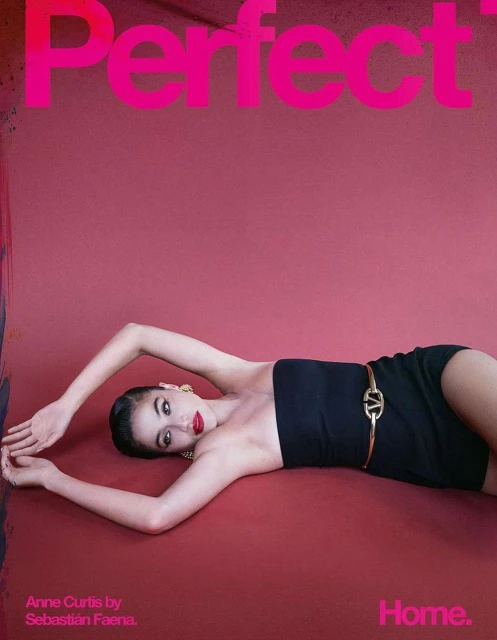 A young woman with dark hair and red lipstick reclines on a red surface, wearing a strapless black top and gold accessories, in a studio setting.