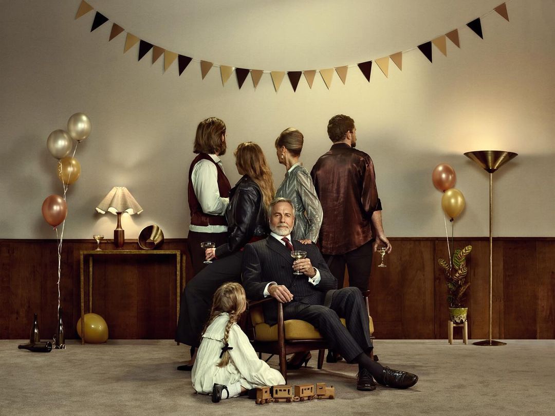 Group shot of formally dressed people gathering in a living room setting with mid-century modern design and a child playing on the floor.