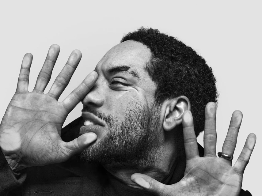 Close-up portrait of an adult man with dark hair partially obscured by his hands, focusing on his face and hand textures.