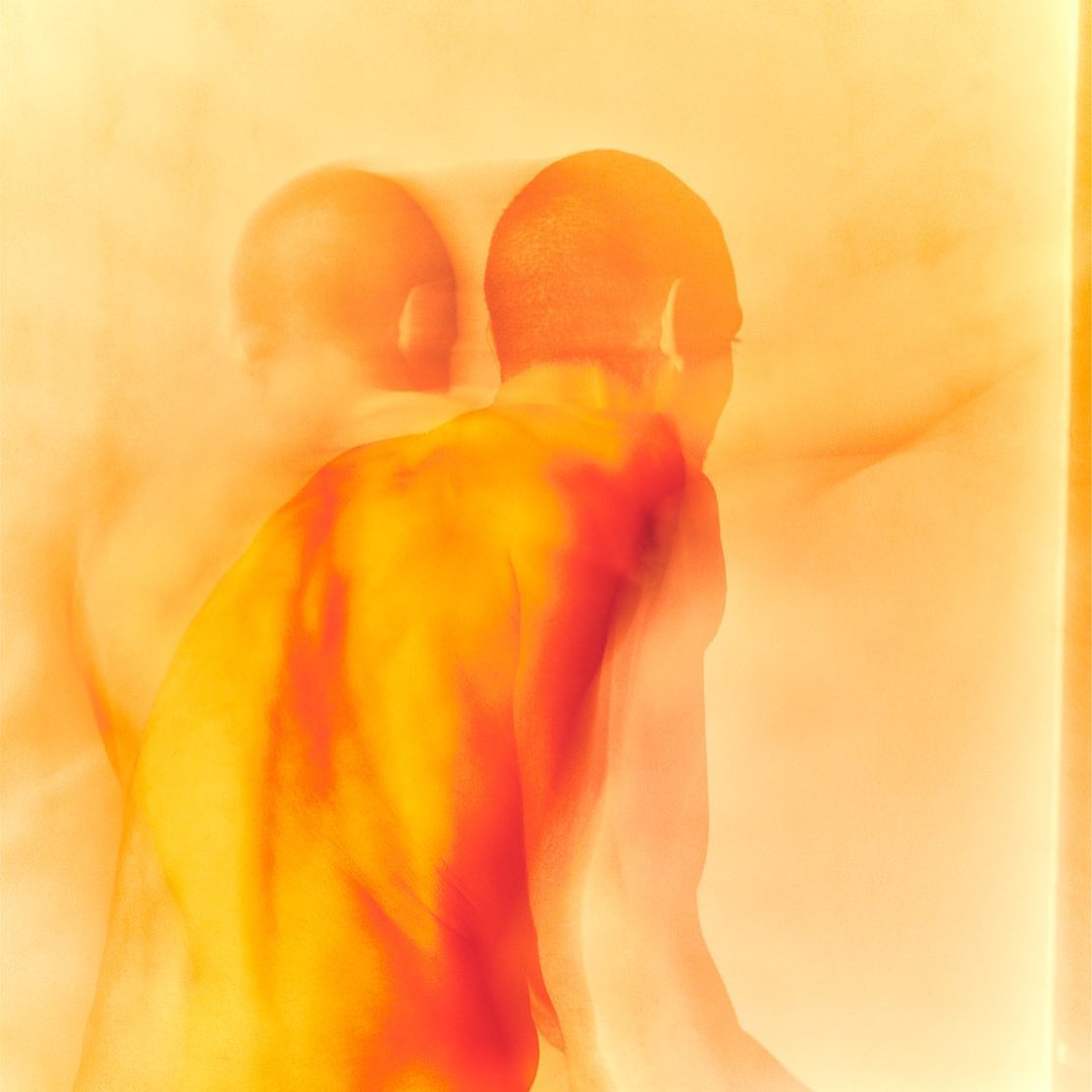 Abstract photograph of a blurry, shirtless adult man with an orange hue and motion blur, evoking a sense of movement and speed.