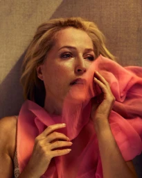 Portrait of a blonde woman in her 50s holding a sheer pink scarf near her face, photographed by Sebastian Nevols.