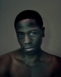 Portrait of a Black man with short dark hair and a neutral expression against a dark background