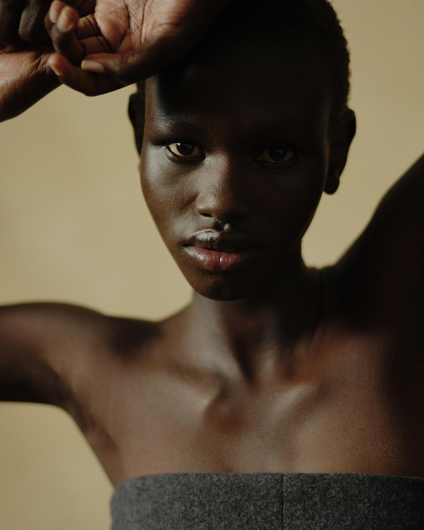 Close-up portrait of a woman with dark skin and a gray strapless top, casting a shadow over her face in a dimly lit indoor setting.