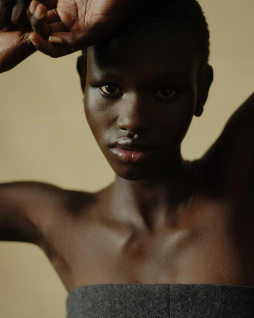 Close-up portrait of a woman with dark skin and a gray strapless top, casting a shadow over her face in a dimly lit indoor setting.
