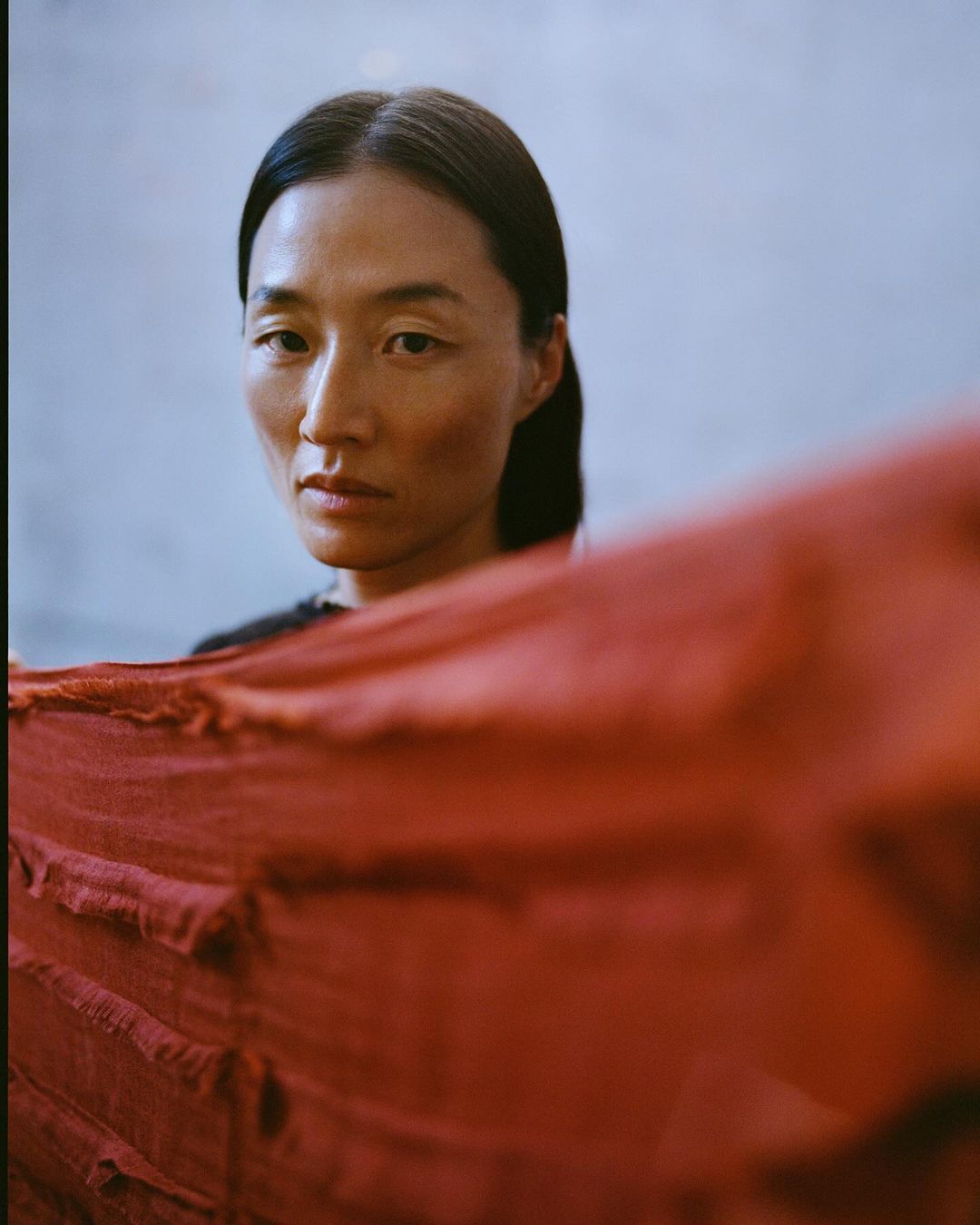 Portrait of an Asian woman indoors with red fabric. The woman faces forward and looks directly at the camera with a serious expression.