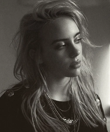 Portrait of Billie Eilish with layered chains wearing a dark top against a plain background photographed by Sebastian Sabal-bruce.