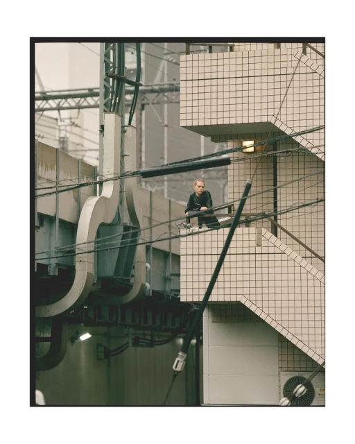 Eye-level shot of a person sitting on a rail in an urban setting with concrete structures and industrial elements in the background.