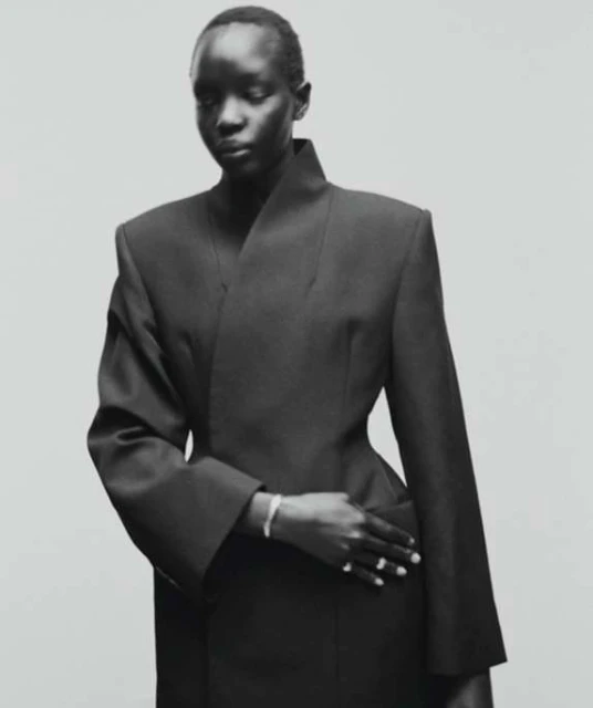 Elegant studio shot of a black model in a chic, dark jacket with sharp lines, set against a neutral background. Classic fashion portrait.