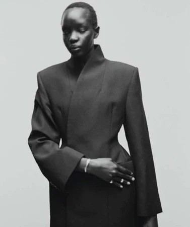 Elegant studio shot of a black model in a chic, dark jacket with sharp lines, set against a neutral background. Classic fashion portrait.