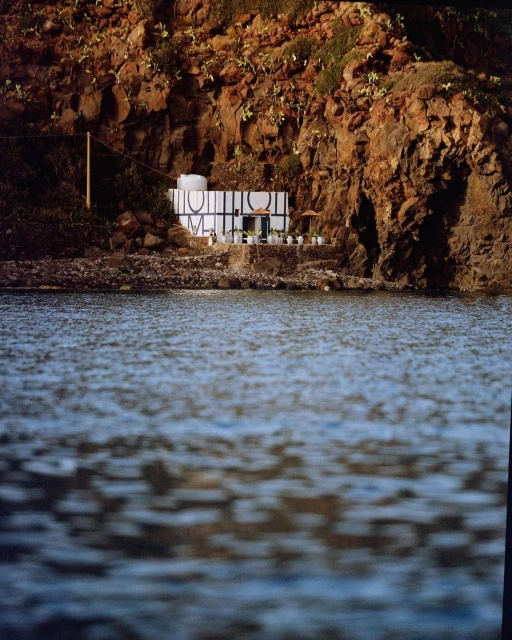 Waterside structure built into a rock face, featuring bold typography and an outdoor setting with calming water ripples.