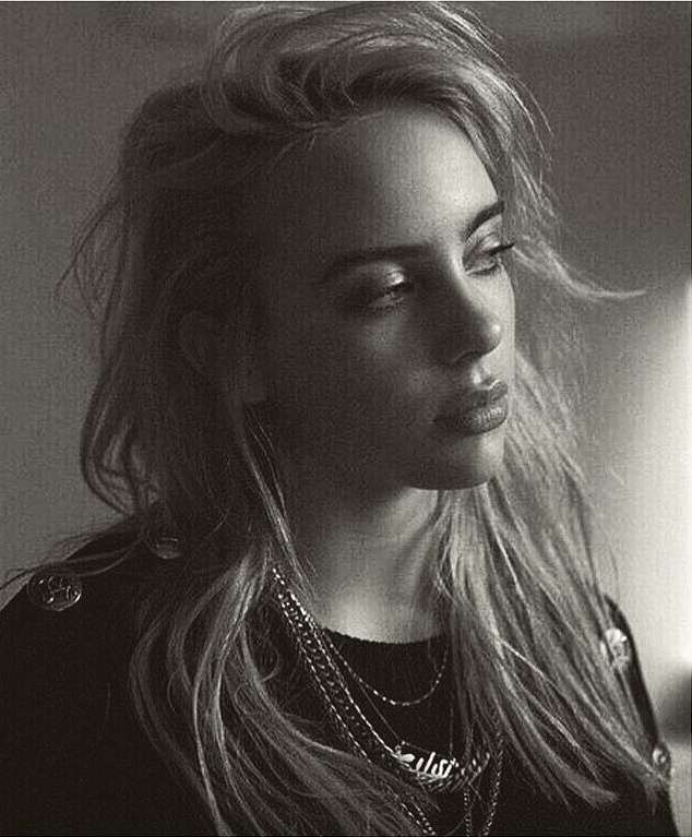 Portrait of Billie Eilish with layered chains wearing a dark top against a plain background